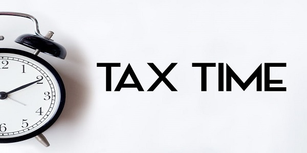 Tax time word written on white office desk table with alarm clock.