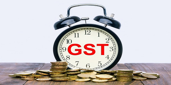 Written word GST Goods and Services Tax on a clock with gold coins on top of a wooden t
