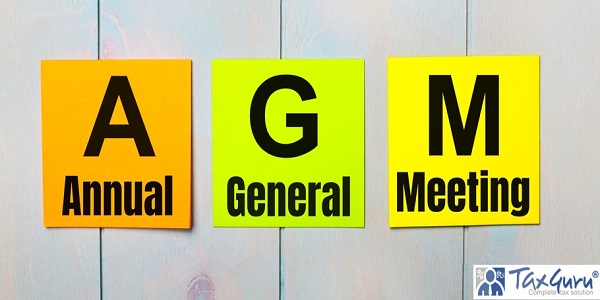 Three colored stickers with the text AGM Annual General Meeting on a light blue wooden background