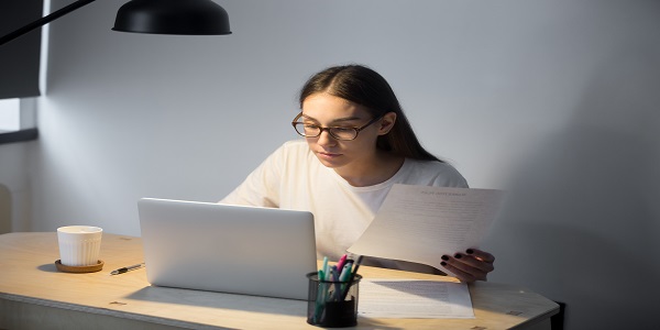 Millennial manager in glasses working on laptop and holding document